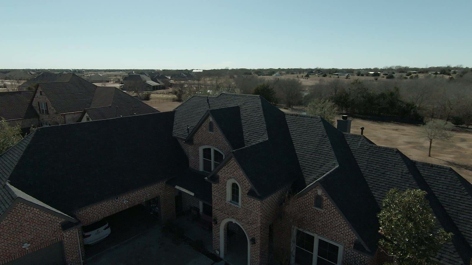 Drone view of a large brick two-story home with a new charcoal architectural shingle roof