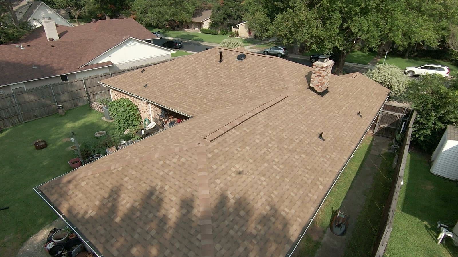 Aerial view of a one-story Dallas home with a finished roof of new brown architectural shingles and a brick chimney