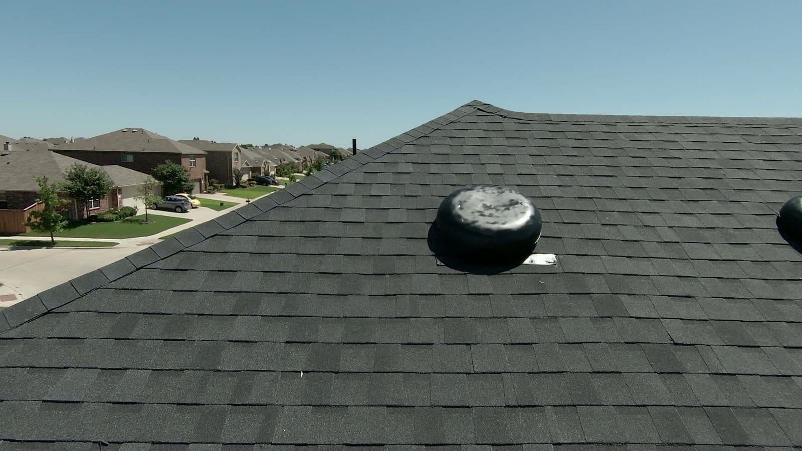 Close drone view of charcoal architectural shingles and a turbine roof vent on a North Texas home